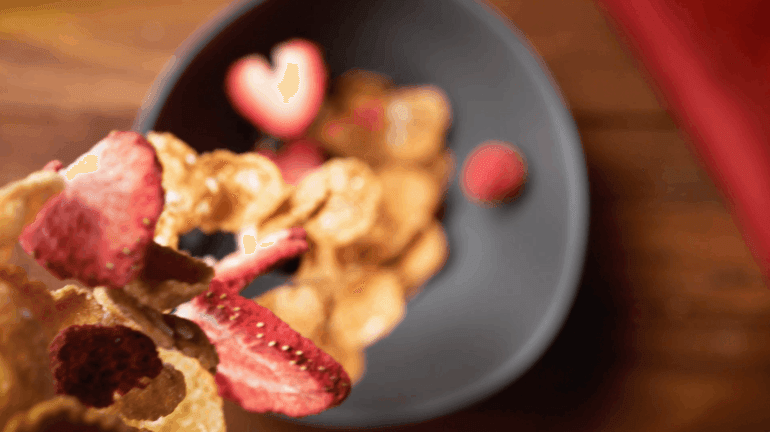 The Triple Berry Oatmeal Crisp flavor being poured into a bowl that awaits below. Some of the cereal is already sitting in the bowl.